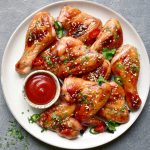 Grilled spicy chicken legs and wings with ketchup on a plate over dark grey slate, stone or concrete background. Top view with copy space.