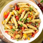 Pasta salad with baked vegetables. Penne pasta with baked peppers, eggplant, pesto and cheese in a white plate on a dark wooden table top view. Italian food. Rustic style.